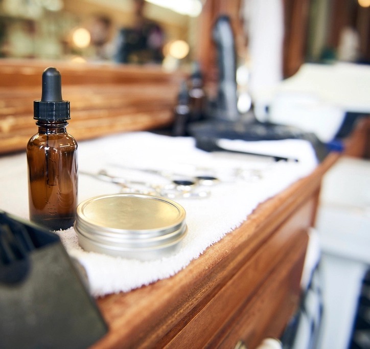 A styling station counter with a dropper bottle, a tin of pomade and shears laid on a white towel