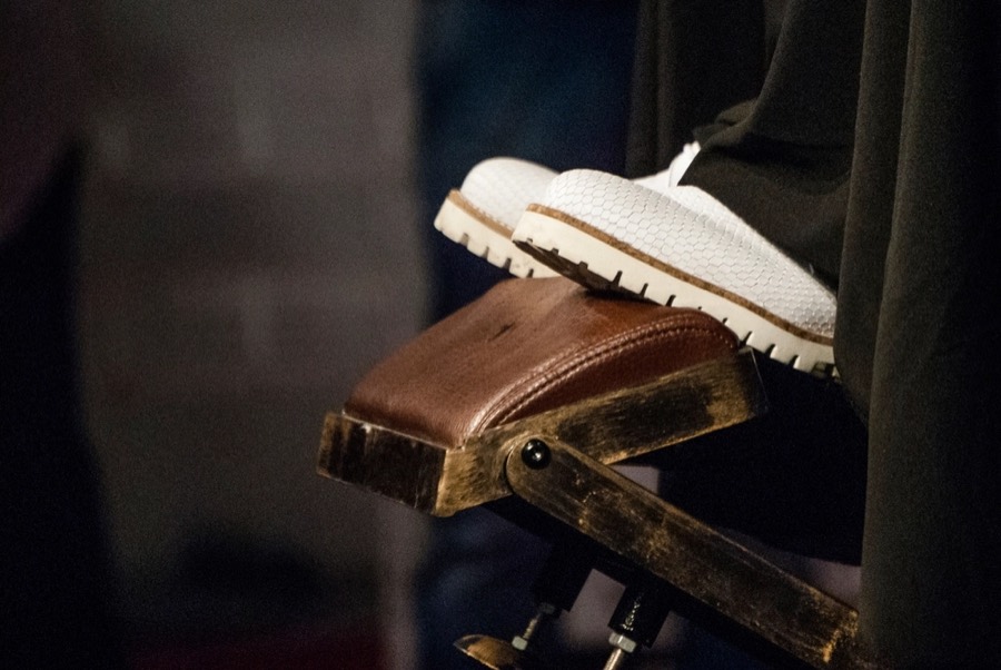 A client's white shoes resting on the brass and leather footrest of a barber chair