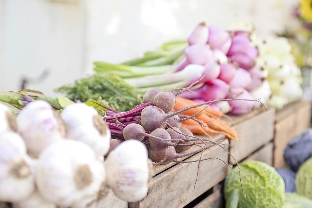 Garlic, beets, carrots and spring onions laid out on wooden crates at a market stall