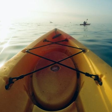 The yellow bow of a sit-in kayak on calm water, other paddlers in the distance