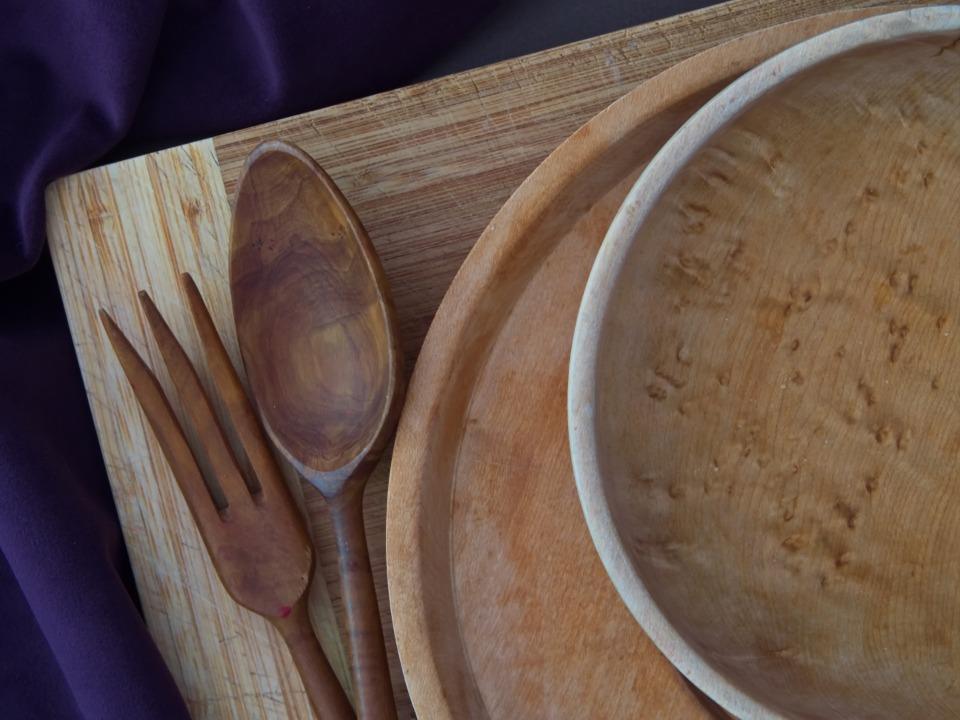 A wooden bowl, plate, spoon and fork laid on a wooden board