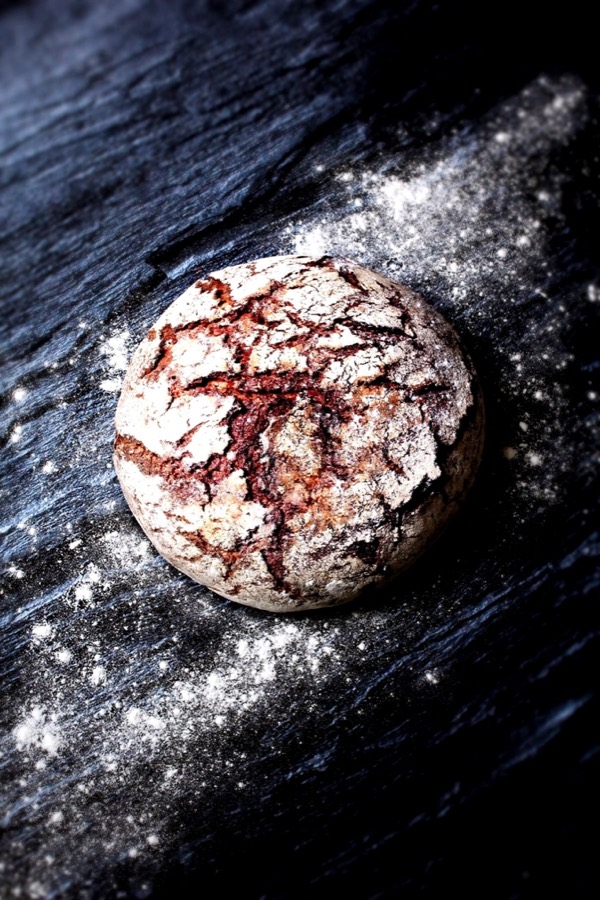 A round crusty loaf with a cracked, flour-dusted top on a dark wooden board