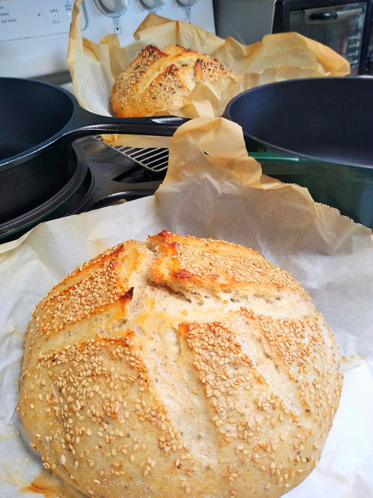 A round sourdough loaf scored in a cross pattern and topped with sesame seeds, cooling on parchment paper