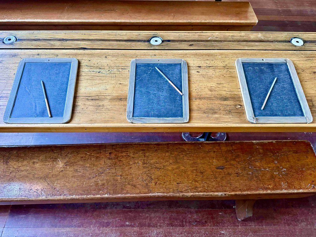 Three slate writing boards with slate pencils resting on an old wooden school desk