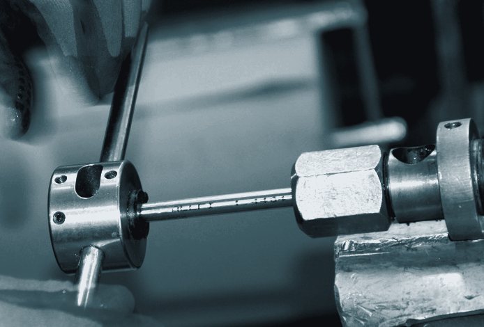 Gloved hands turning a tap handle on a steel part held in a bench vise