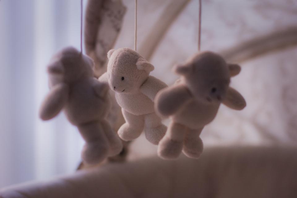 Three soft cream toy lambs hanging from a crib mobile in window light
