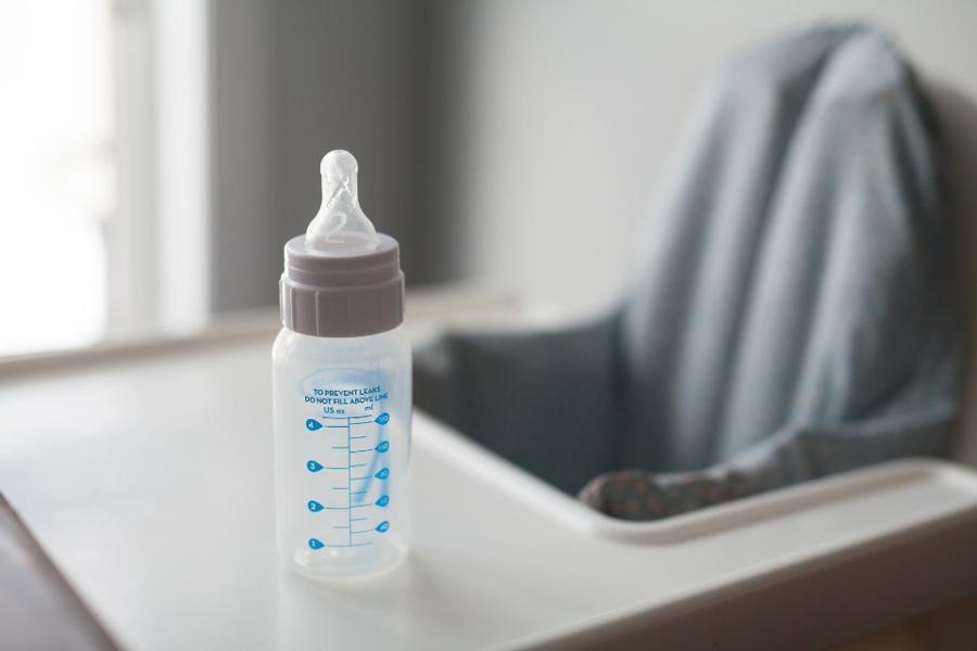 A baby bottle with measurement marks standing on the tray of a white high chair