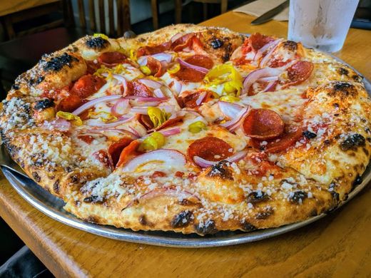 A 16 inch pie with pepperoni cups, sliced red onion and banana peppers on a charred, blistered crust