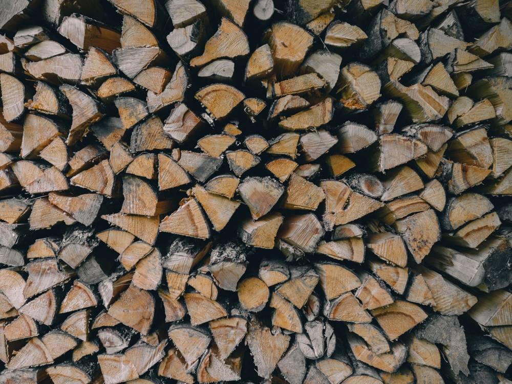 A wall of split firewood stacked end-on, pale cut faces of oak