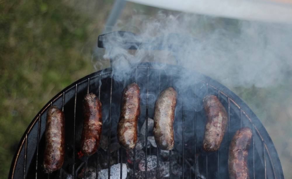 Sausages on a grill grate with smoke drifting up over them