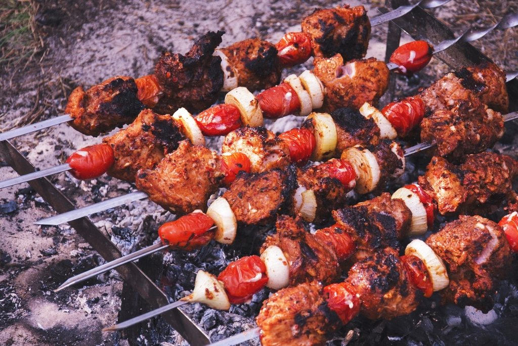 Skewers of marinated meat, tomato and onion charring over a bed of glowing coals