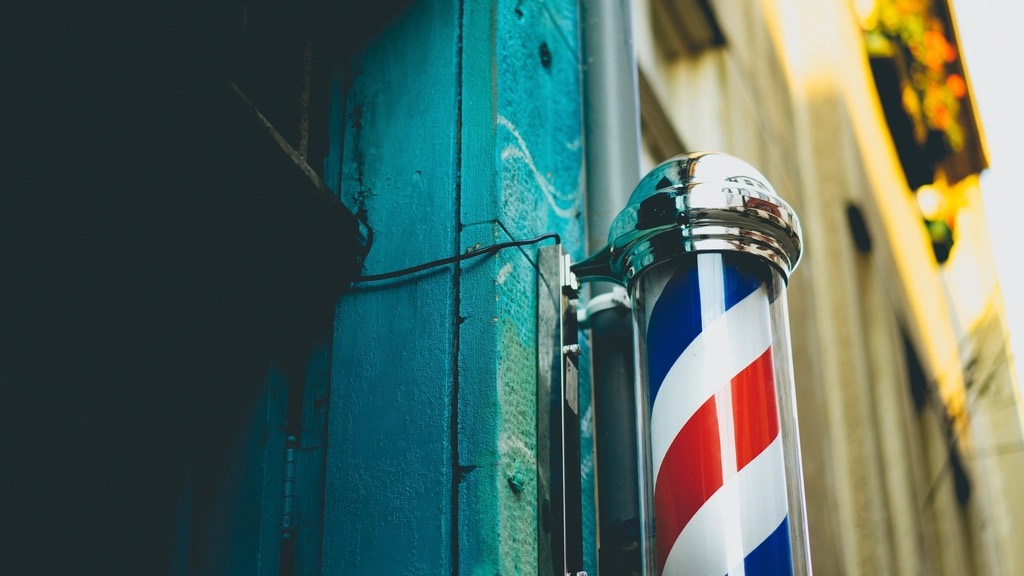 A chrome-capped barber pole with red, white and blue stripes mounted on a teal-painted wall