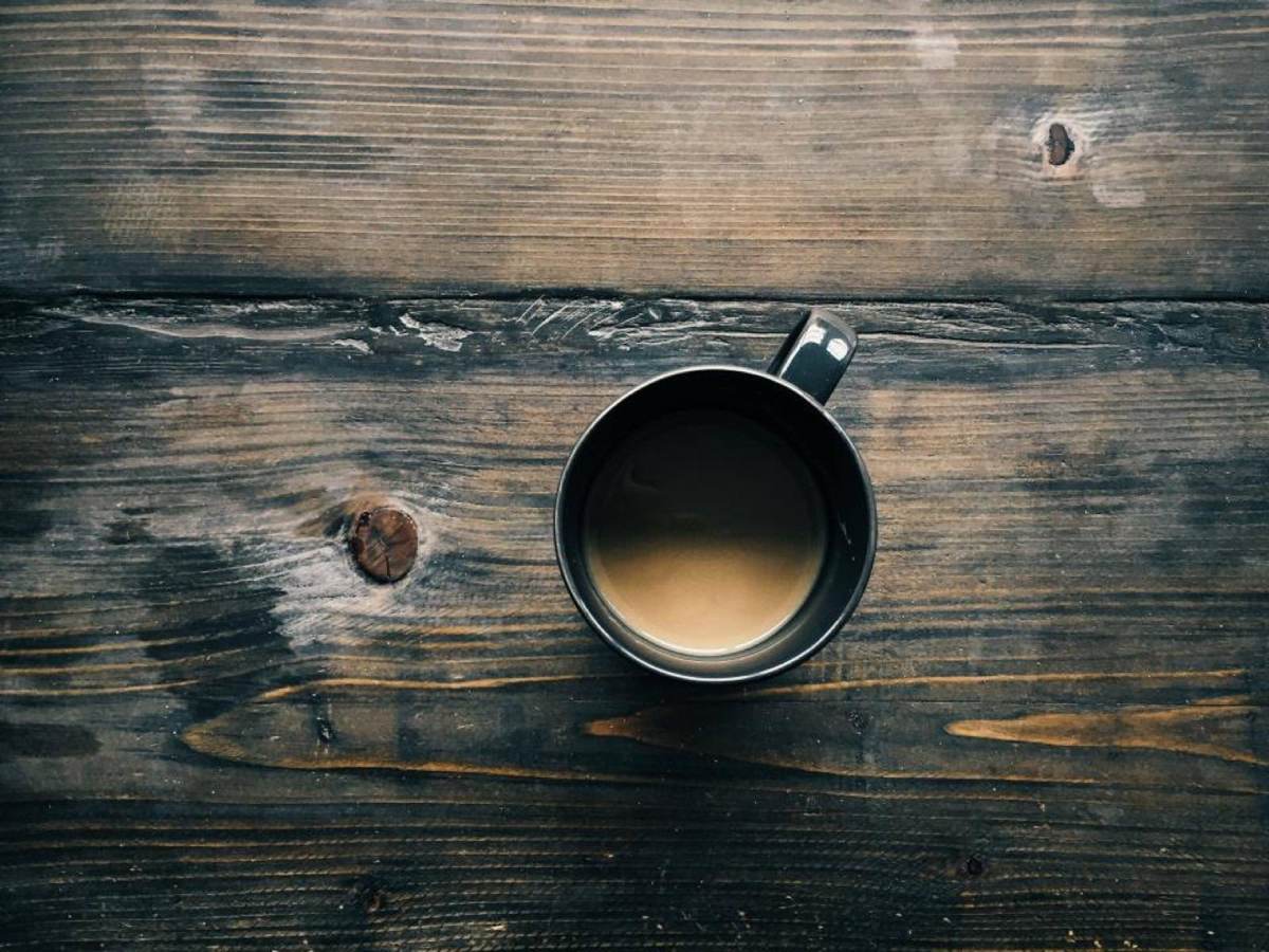 A single mug of coffee with milk on a dark, weathered wooden table, seen from above
