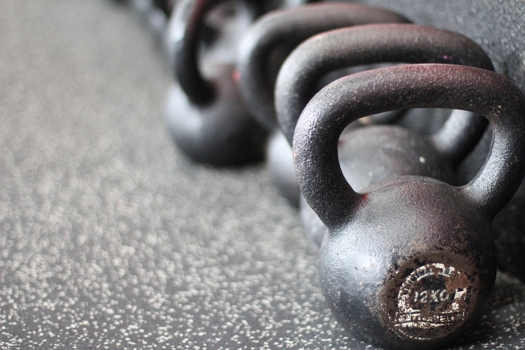 A row of worn cast iron kettlebells on a speckled rubber floor