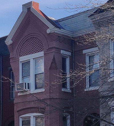 Front of a red brick rowhouse with a bay window and white cornice