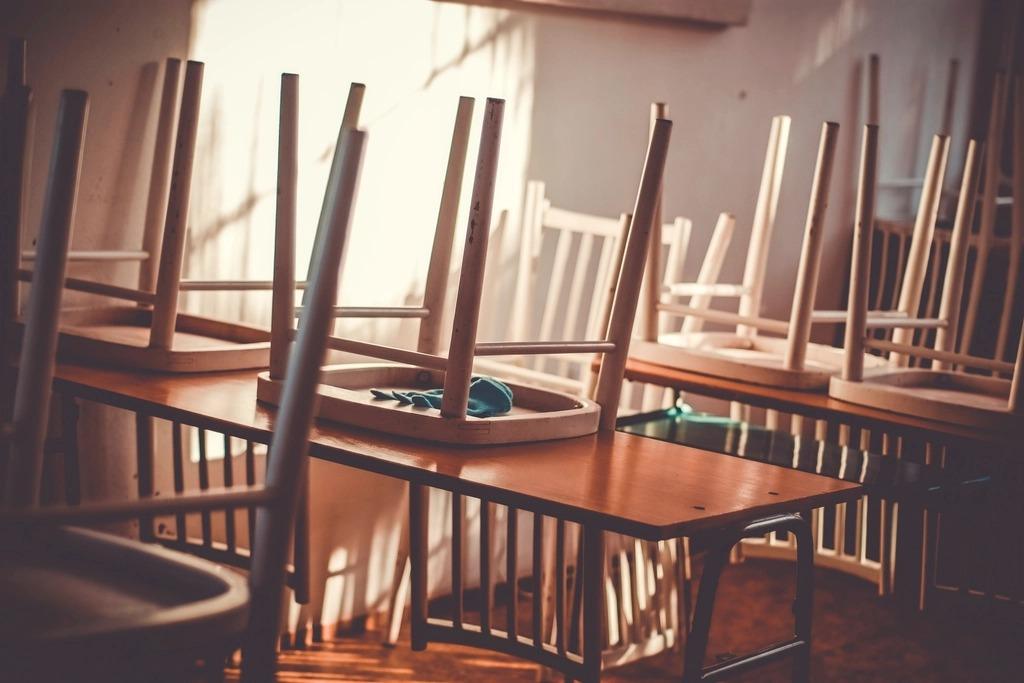 Small wooden chairs turned upside down on classroom tables in late afternoon sun