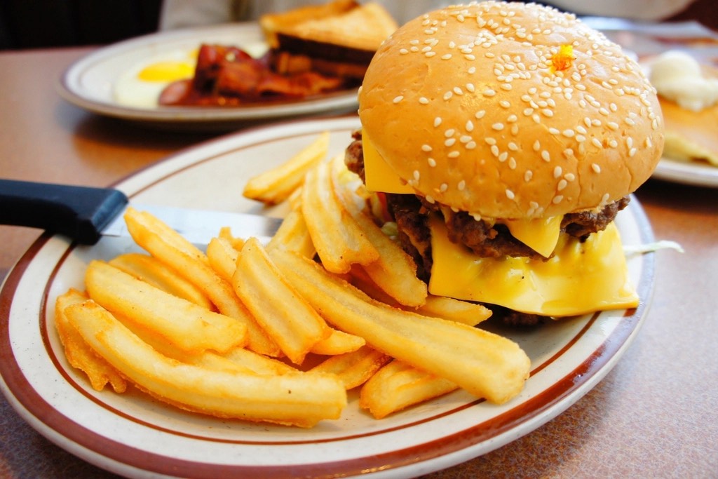 A double cheeseburger with two thin patties and melted American cheese on a sesame bun, next to fries