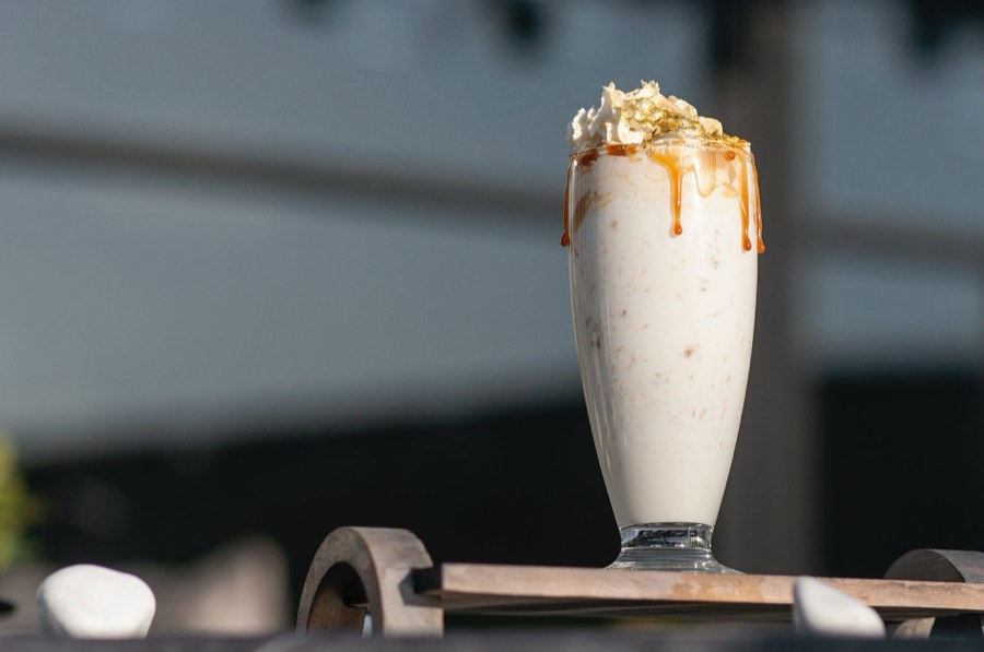 A tall glass of vanilla milkshake topped with whipped cream and a caramel drizzle