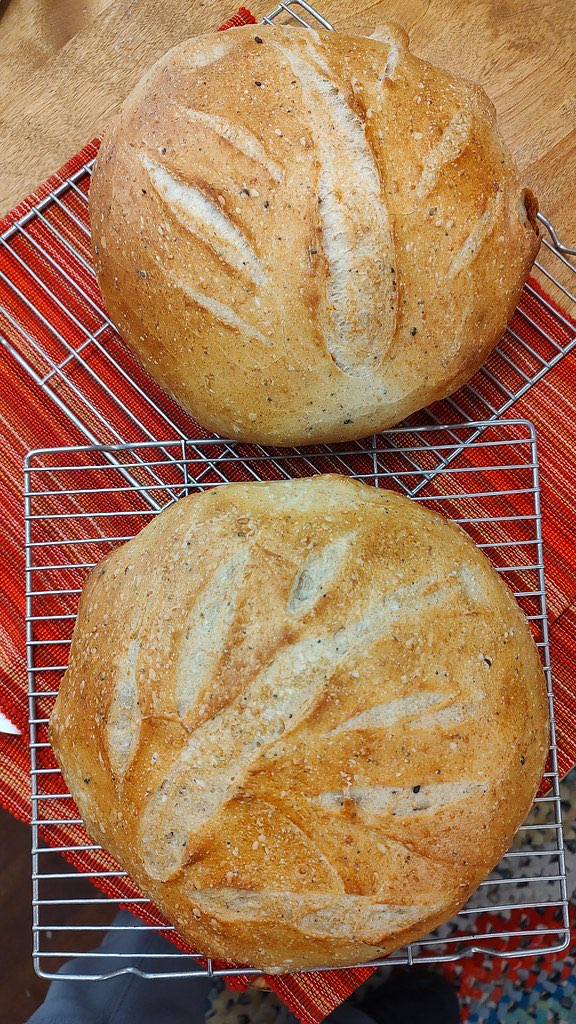 Two round scored sourdough loaves cooling on wire racks over a striped red cloth, seen from above