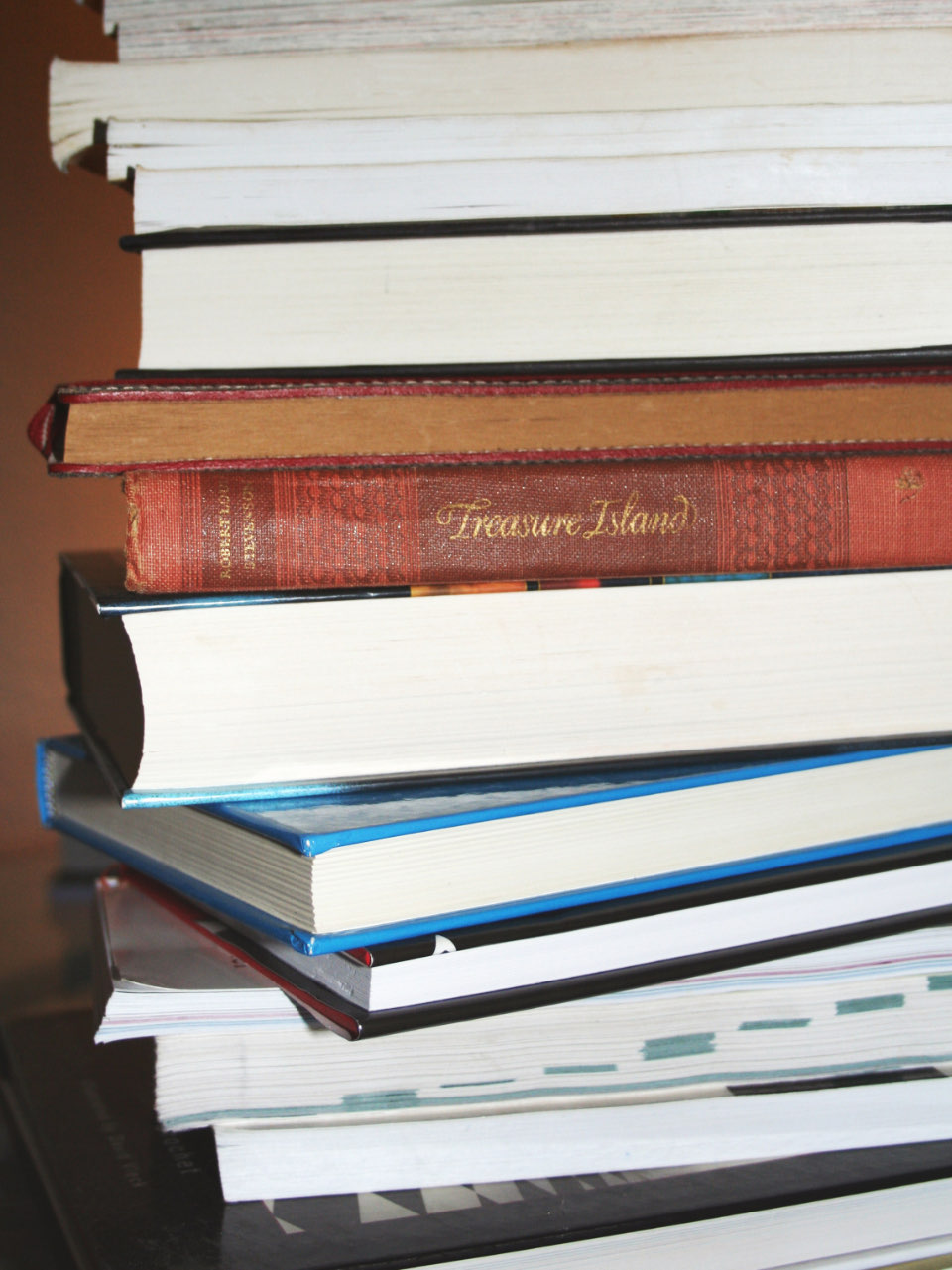 A tall stack of hardback and paperback books, with a red cloth copy of Treasure Island in the middle