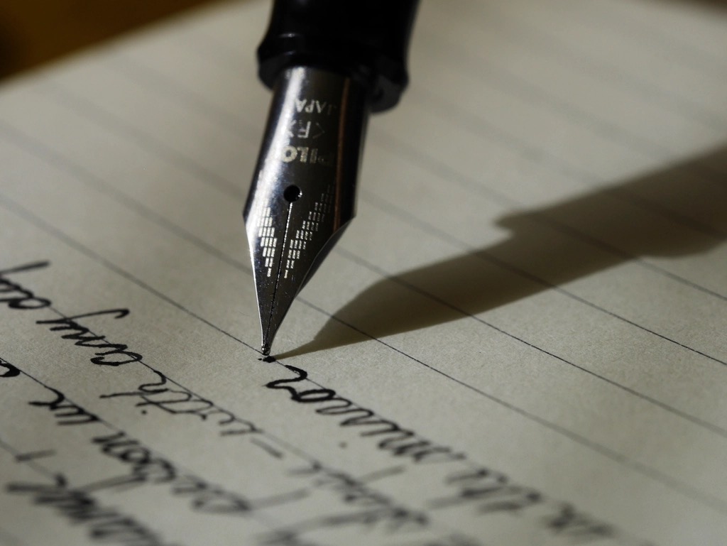 Close view of a fountain pen nib writing a line of cursive on ruled paper
