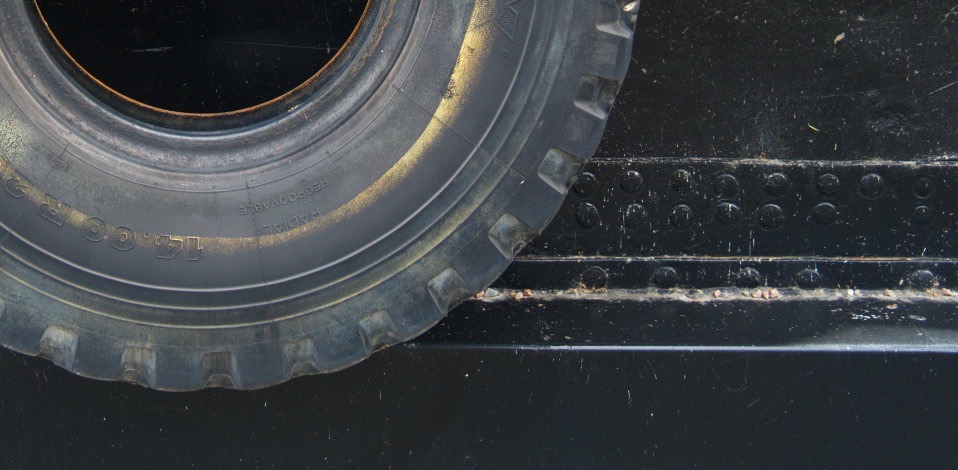 A large off-road truck tire with deep lugs resting against a black steel deck