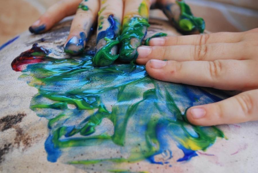 Hands spreading green and blue finger paint across a sheet of paper