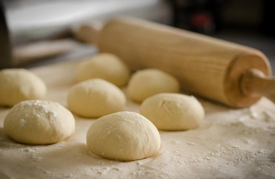 Rounded balls of pizza dough resting on a floured wooden counter, a rolling pin behind them