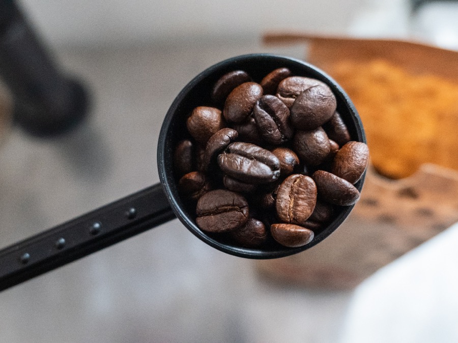 A black measuring scoop heaped with dark roasted coffee beans