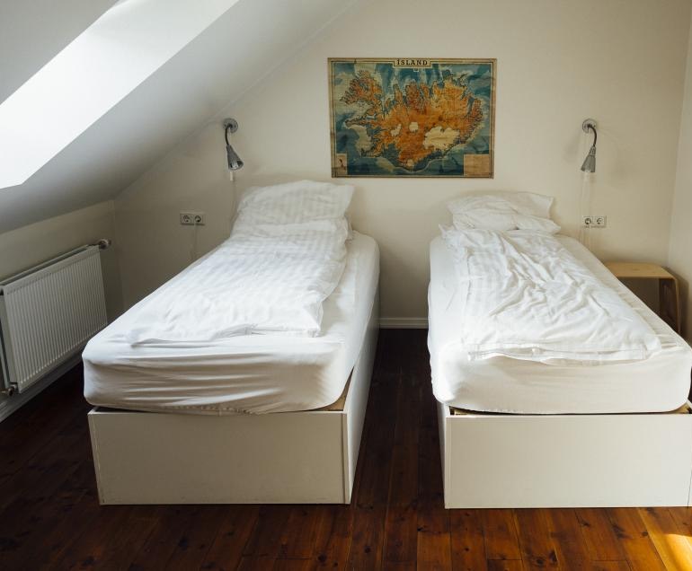 Two made-up twin beds side by side under a sloped attic ceiling, on dark wood floors