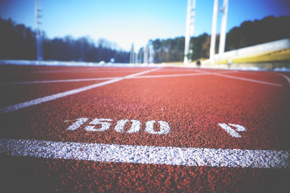 Low view along a red running track with white lane lines and a painted 1500 metre start marking