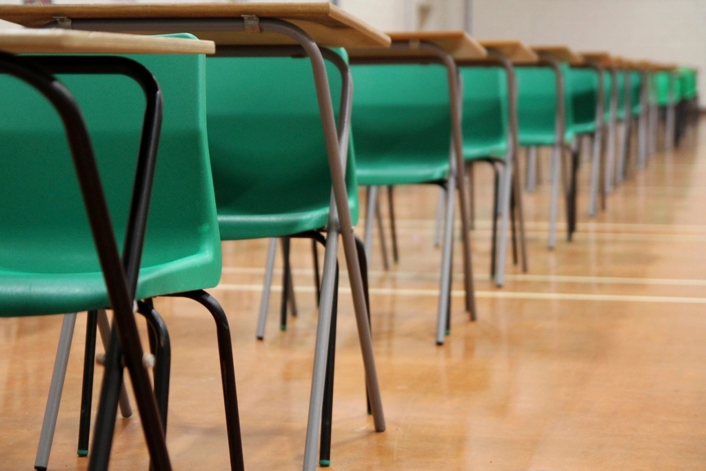 Rows of empty desks and green chairs set out in a hall, ready for an exam